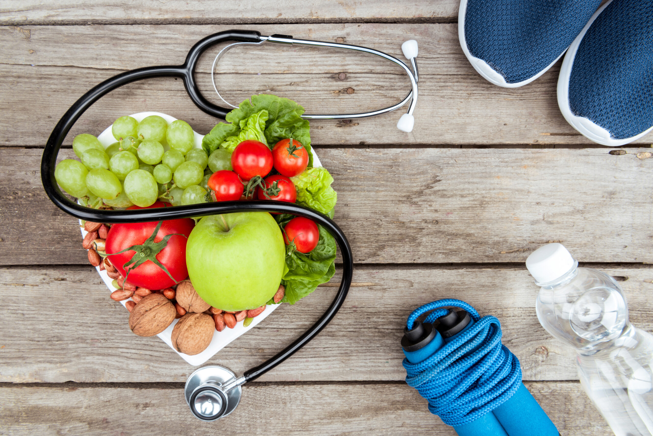 top view of stethoscope, organic vegetables and fruits and sport equipment on wooden surface,